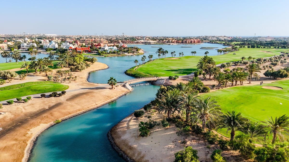 Expansive aerial view of a luxury golf resort with surrounding town and lagoons