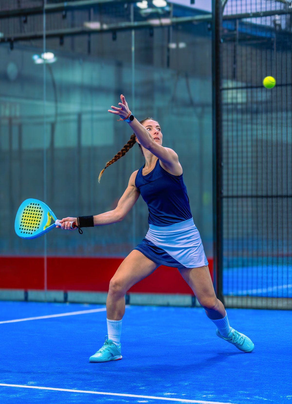 An athletic woman in blue sportswear prepares for a groundstroke on a padel court