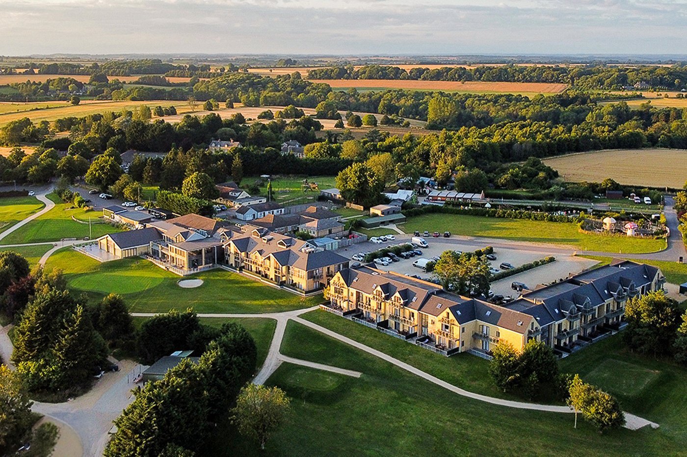 Aerial view of a large residential complex with multiple brick buildings, manicured lawns, and parking areas surrounded by countryside farmland