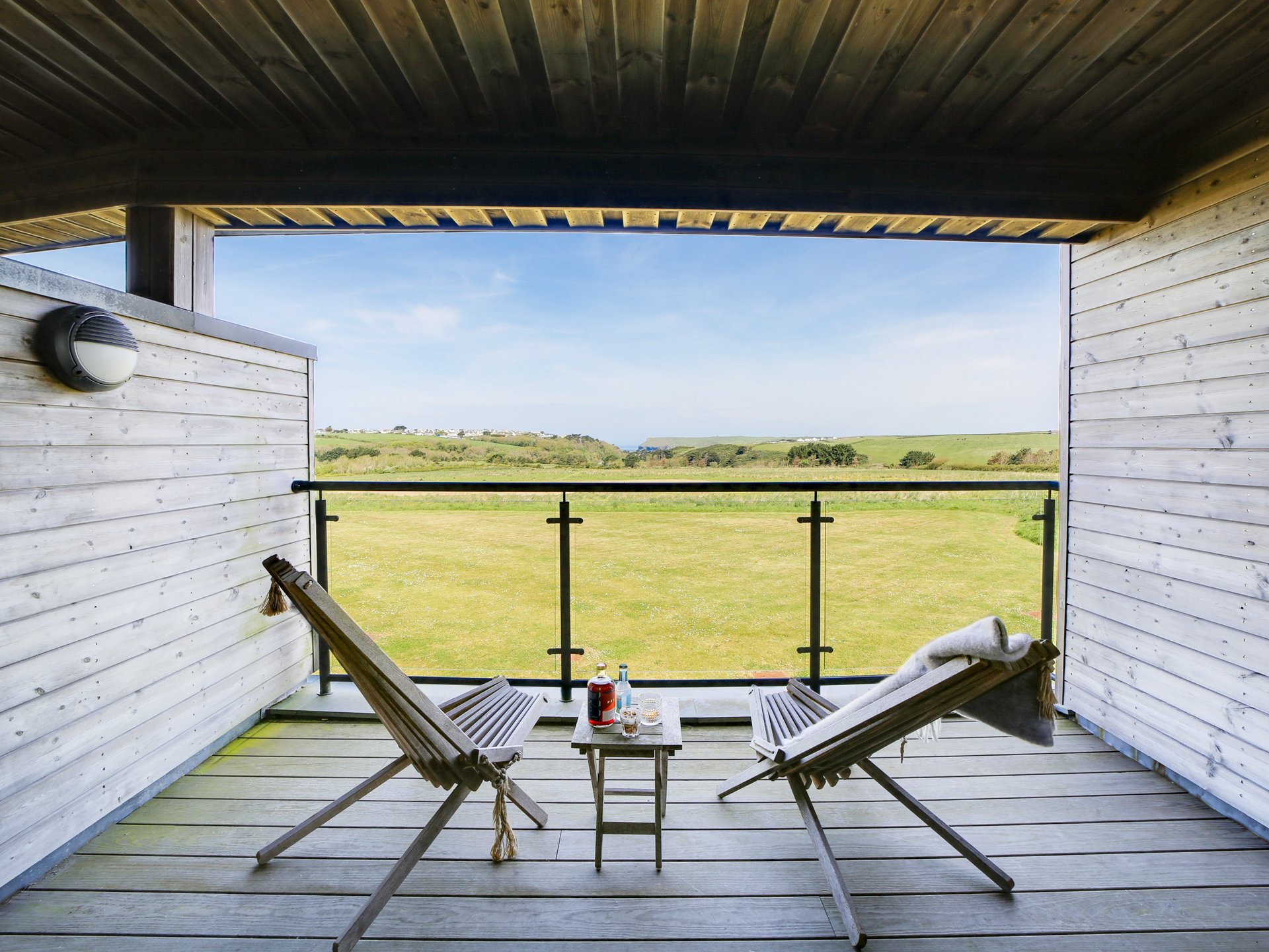 Two lounge chairs on a modern deck overlooking a vast green field under a clear sky