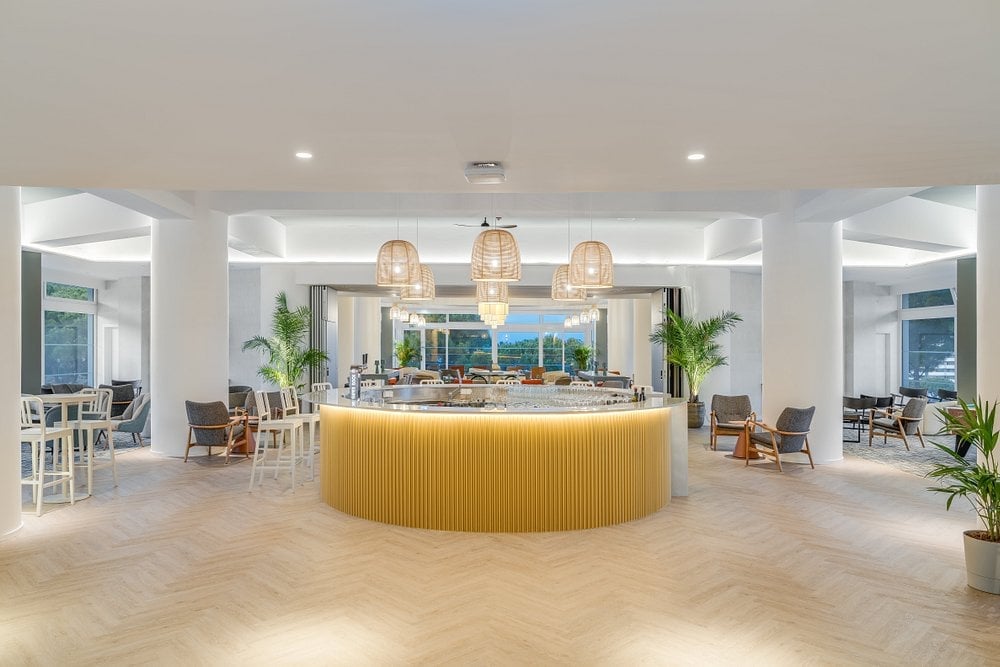 Modern luxury hotel lobby with a large curved golden reception desk, pendant lighting, potted plants, and seating areas overlooking ocean views