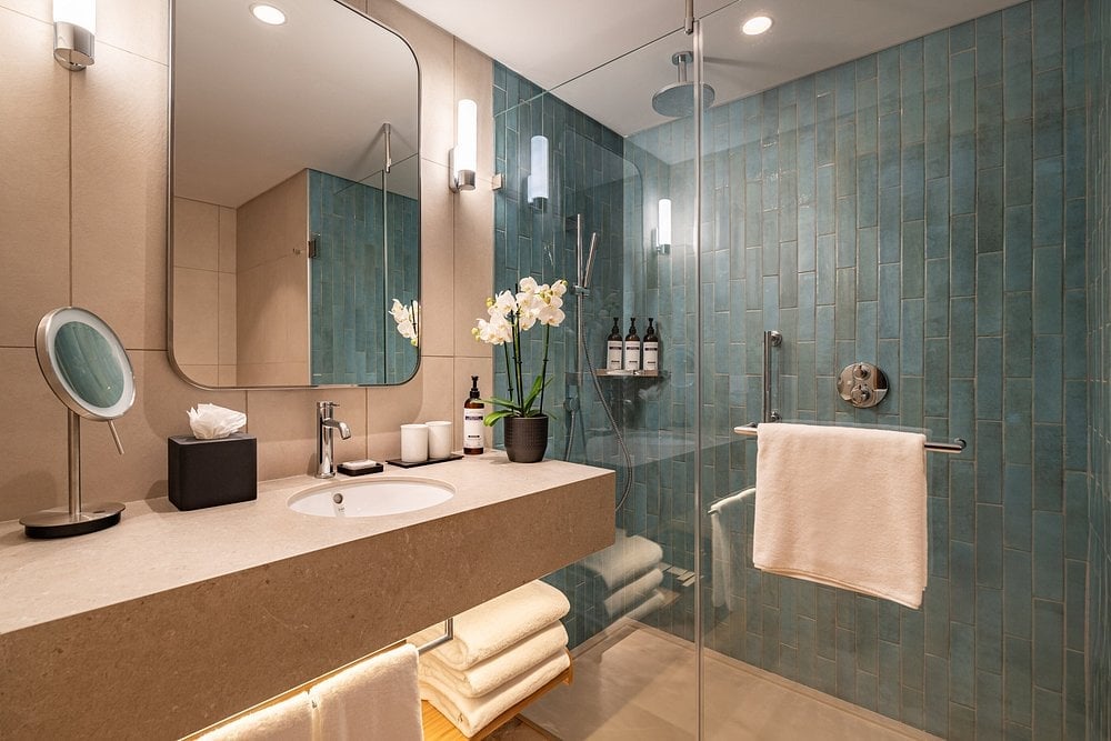 Modern bathroom with floating vanity, large mirror, teal subway tile shower enclosure, and contemporary fixtures