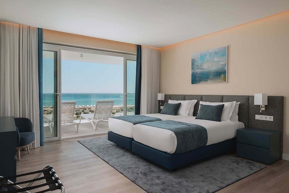 Modern beachfront bedroom with king bed, ocean view balcony, floor-to-ceiling windows, and contemporary furnishings