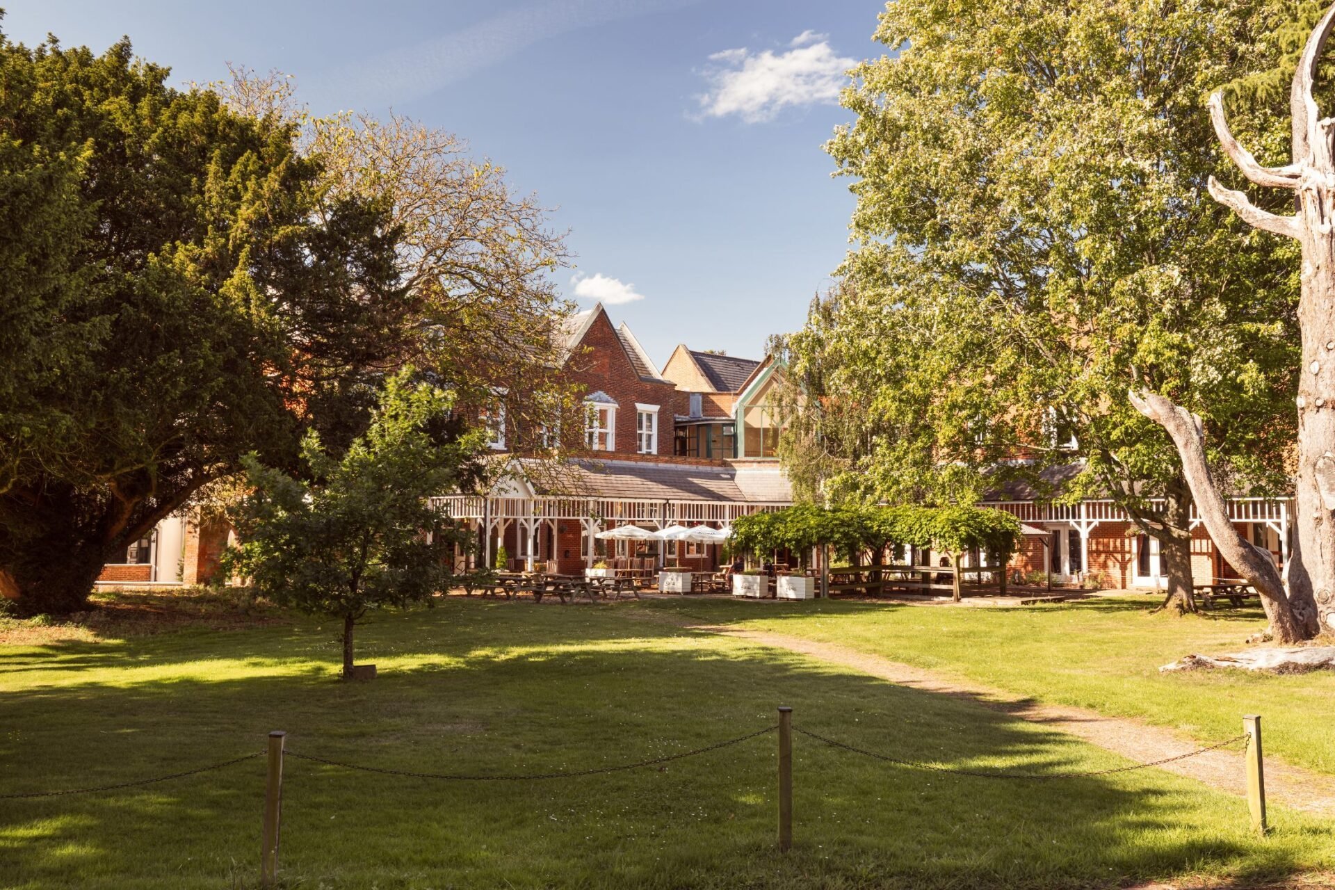 Victorian brick mansion surrounded by mature trees and manicured green lawn on a sunny day