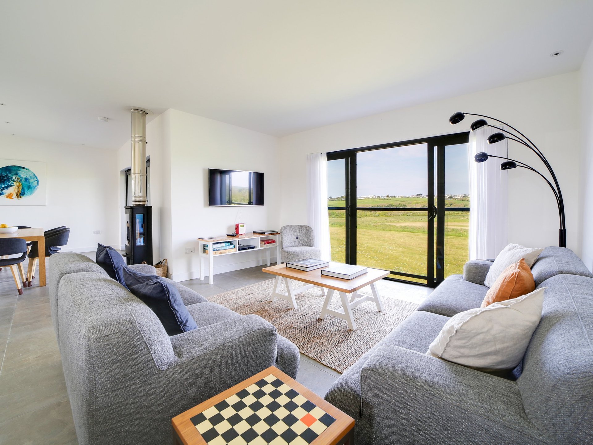 Modern living room with two gray sofas, coffee table, fireplace, and large windows overlooking green fields