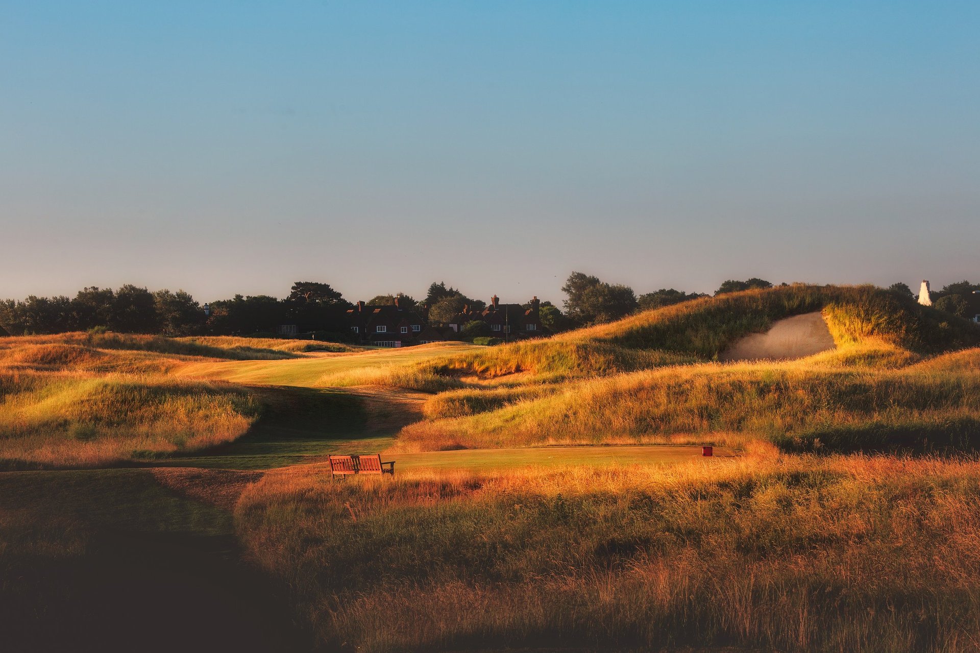 Golden rolling hills covered in dry grasses at sunset with a farmhouse in the distance and clear blue sky