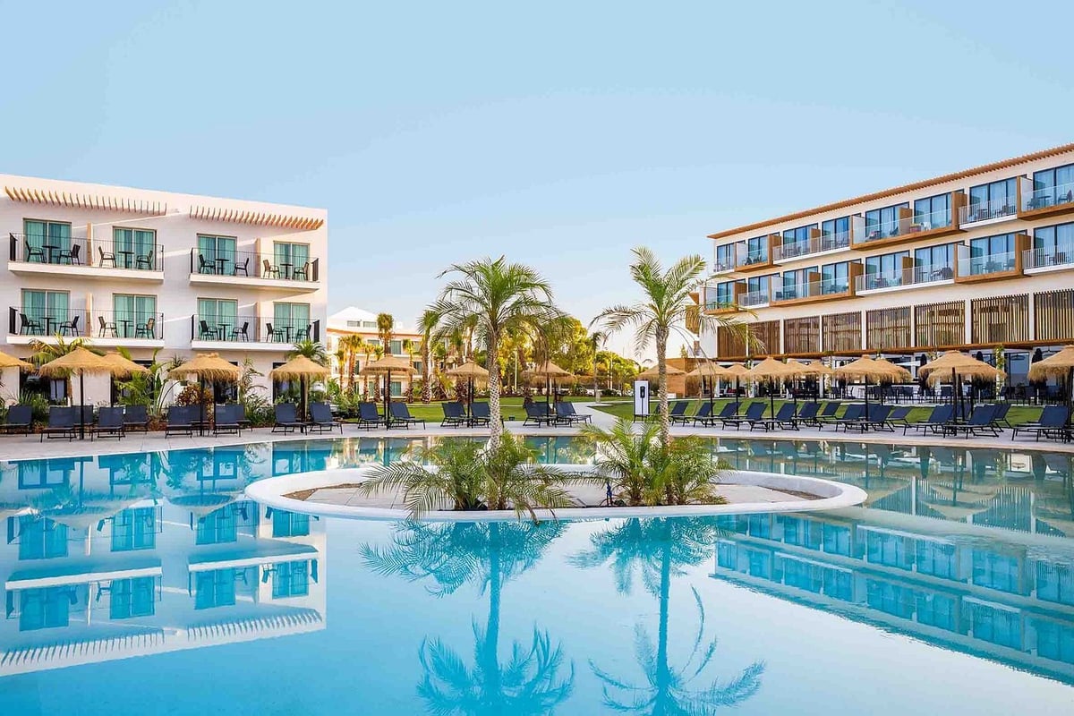 Luxury resort with large swimming pools, palm trees, and beige hotel buildings under clear blue sky