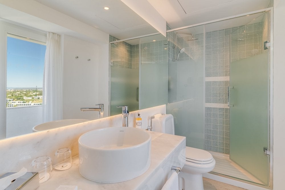 Modern bathroom with white circular sink, glass shower enclosure, and window overlooking city skyline