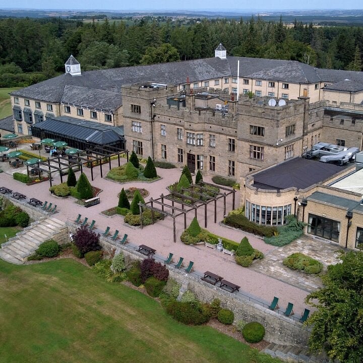 Aerial view of a large stone hotel or resort with manicured grounds, surrounded by forests and countryside landscape
