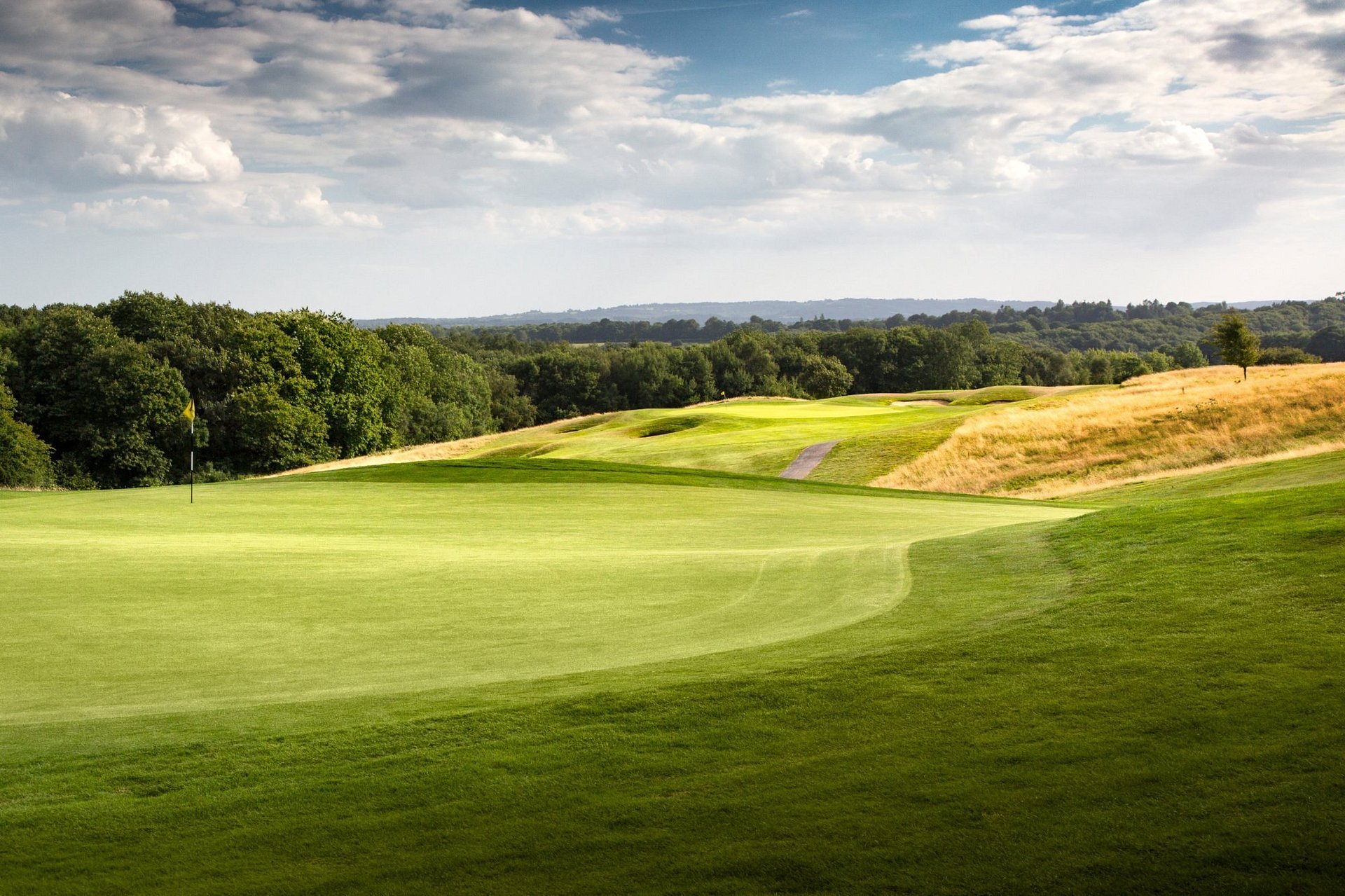 Scenic golf course with manicured green fairway, sand bunker, tree-lined background, and cloudy sky