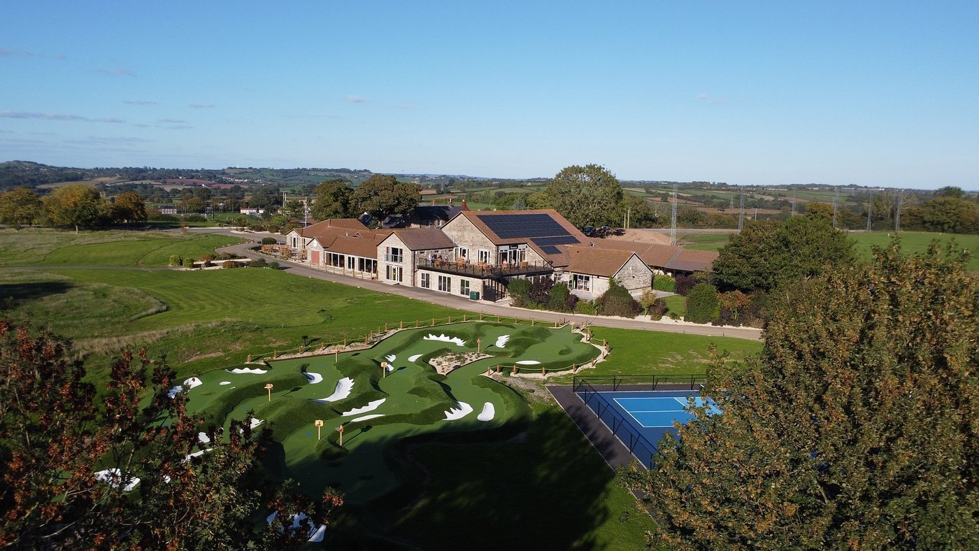Aerial view of a large residential estate with mansion, manicured grounds, putting green, and swimming pool surrounded by landscaping