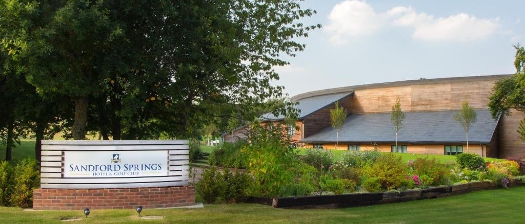 Sandford Springs entrance sign with manicured grounds, green lawn, and modern building with sloped roof visible in the background