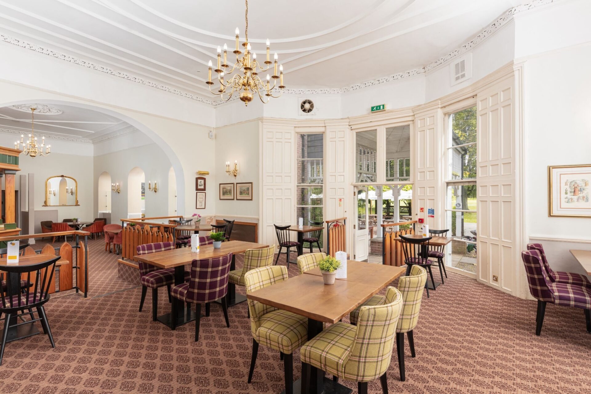 Elegant dining room with multiple tables, plaid chairs, chandelier, white columns, and framed artwork on walls