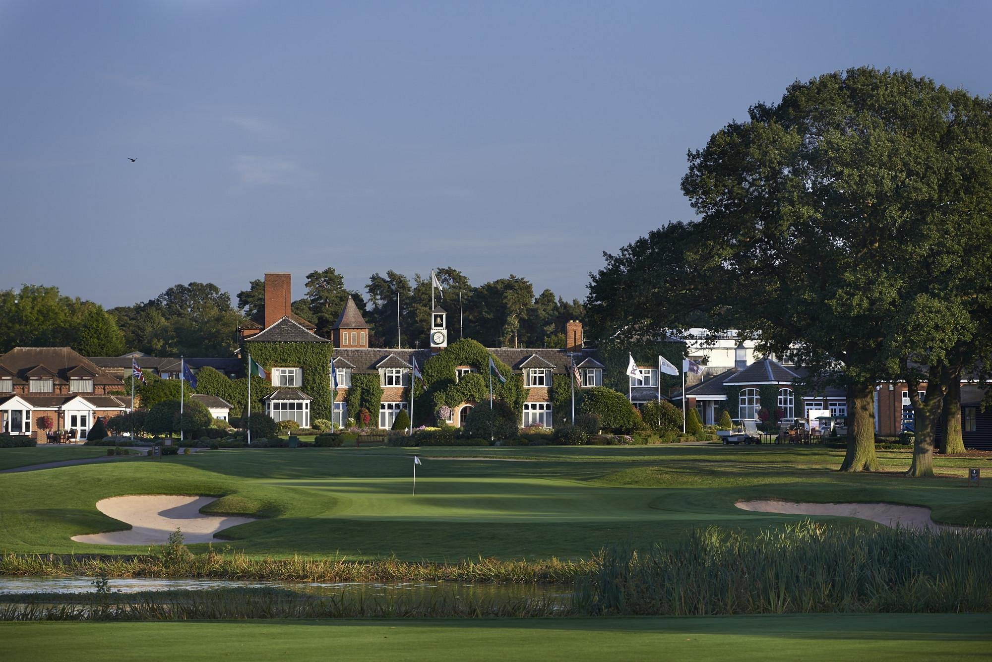 Golf course with manicured greens, sand bunker, and row of elegant residential buildings along the fairway under blue sky
