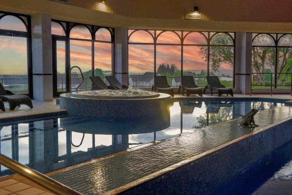 Modern indoor pool with hot tub overlooking sunset mountain landscape through large windows