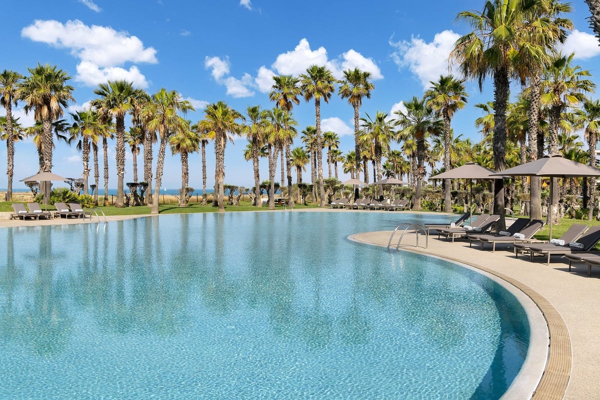 Resort pool with turquoise water, loungers, and palm trees under blue sky with white clouds