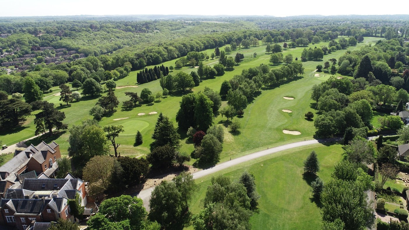 Aerial view of a golf course with green fairways, scattered trees, sand bunkers, and residential homes on the perimeter