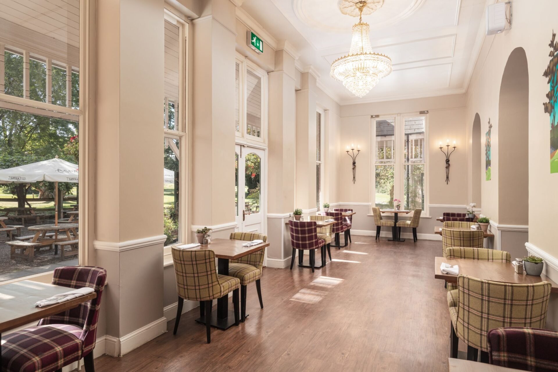 Elegant hotel lounge with high ceilings, plaid seating, pendant lights, and large windows overlooking gardens