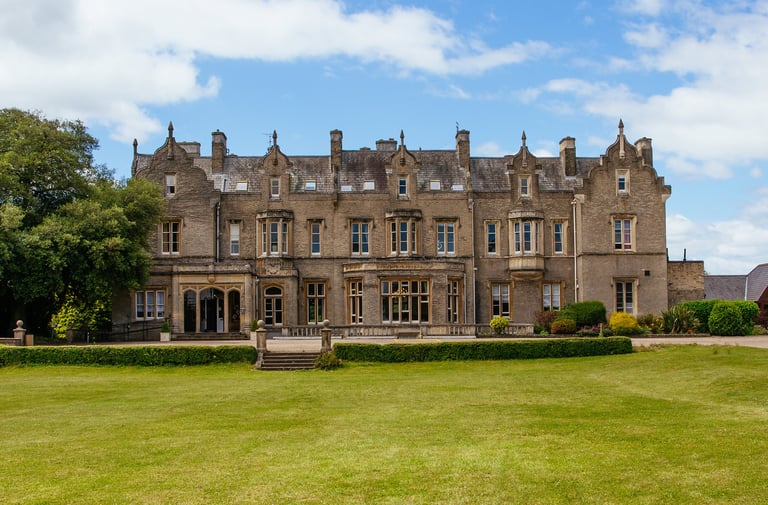 Grand Victorian stone mansion with manicured lawn and blue sky