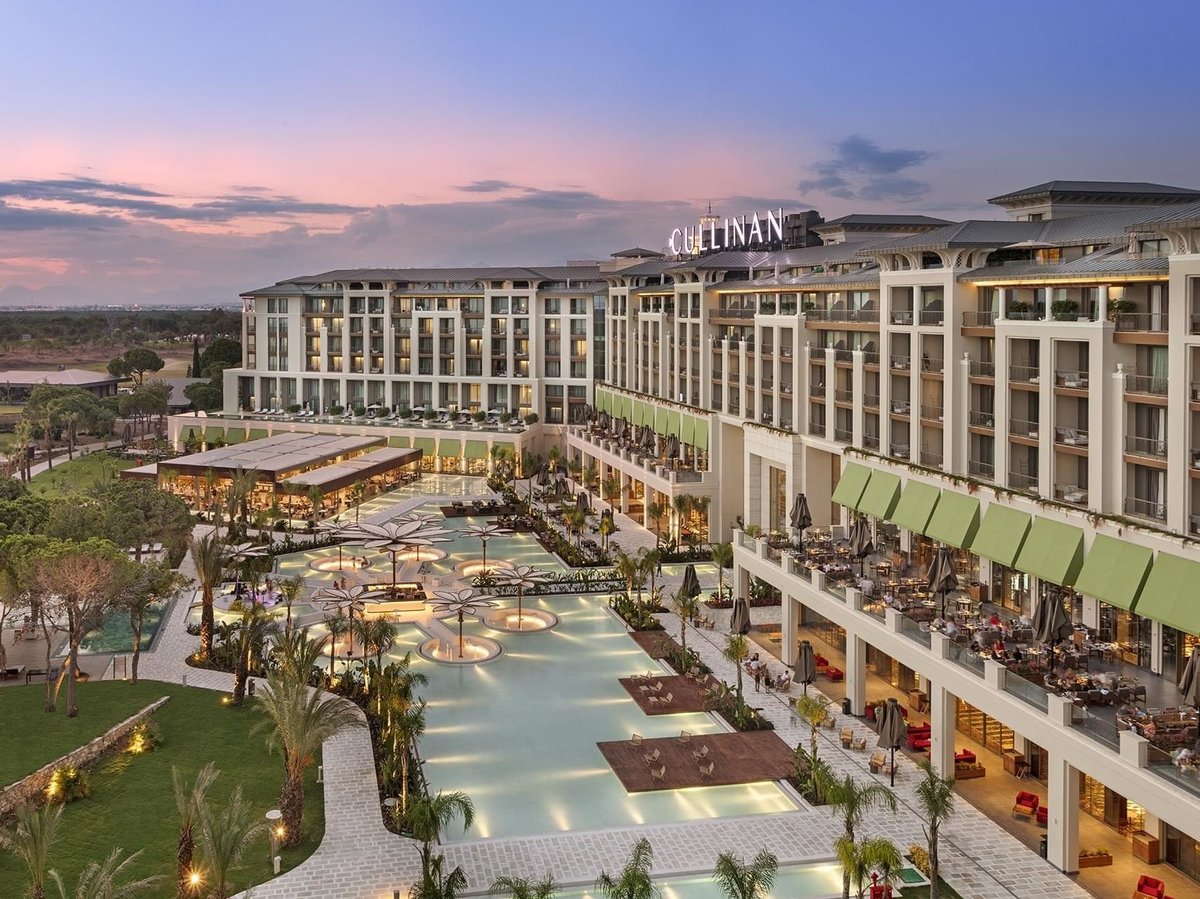 Luxurious resort hotel with illuminated pool courtyard, landscaping, and modern architecture at twilight
