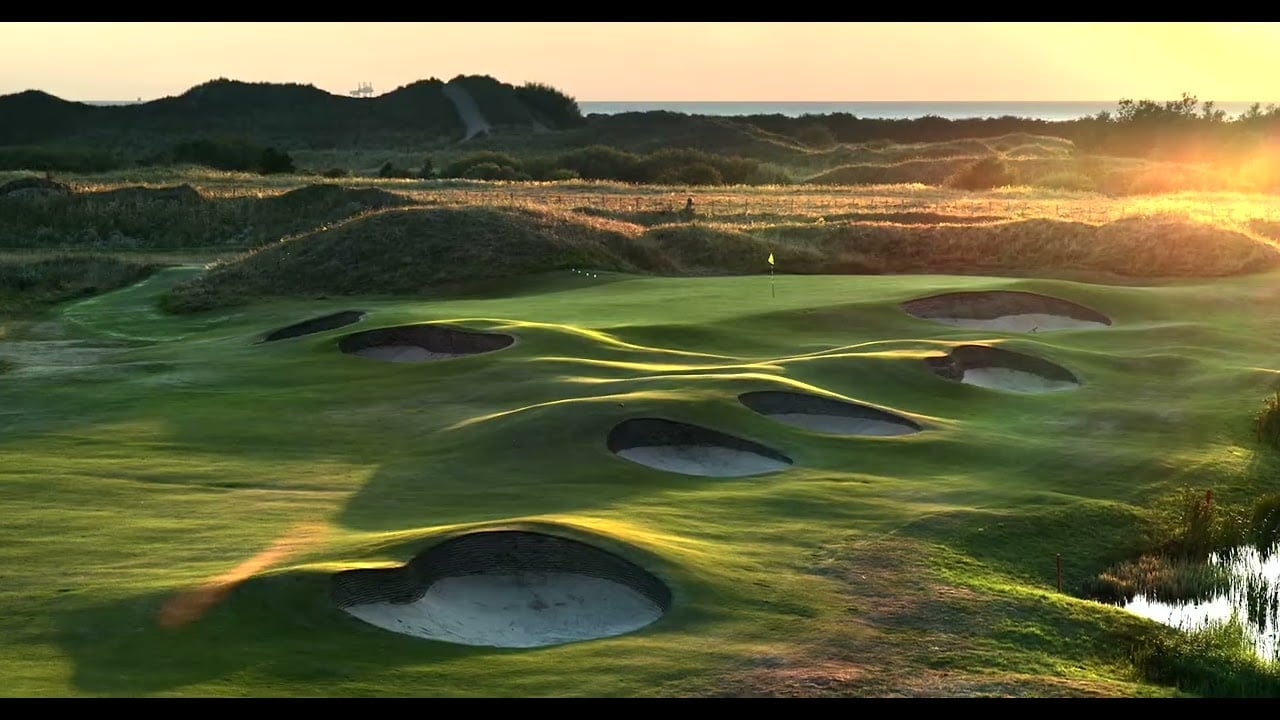 Golf course with multiple bunkers at golden sunrise, rolling green fairways with bunkers, and distant mountains under warm morning light