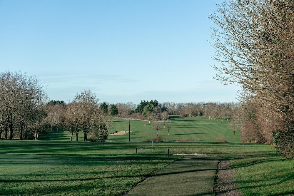 Rolling green golf course with scattered bare trees and a clear blue sky in early spring