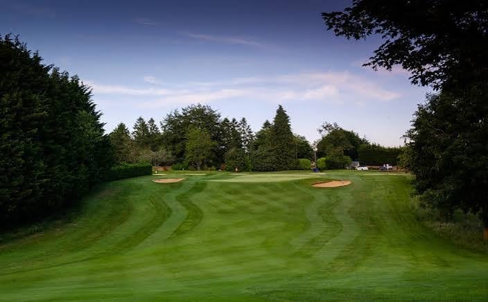 Wide view of a golf course fairway with manicured grass, bunkers, and tree-lined borders under clear blue sky