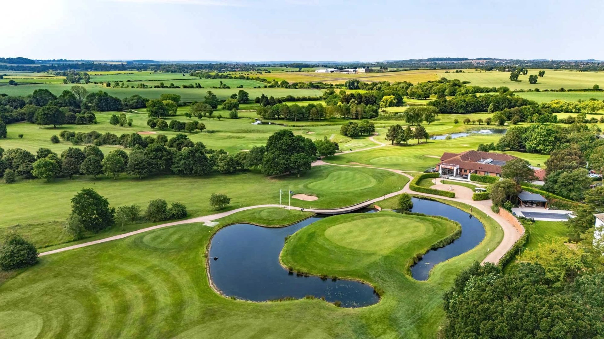 Aerial view of a rural property with winding blue pond surrounded by manicured green fields and trees