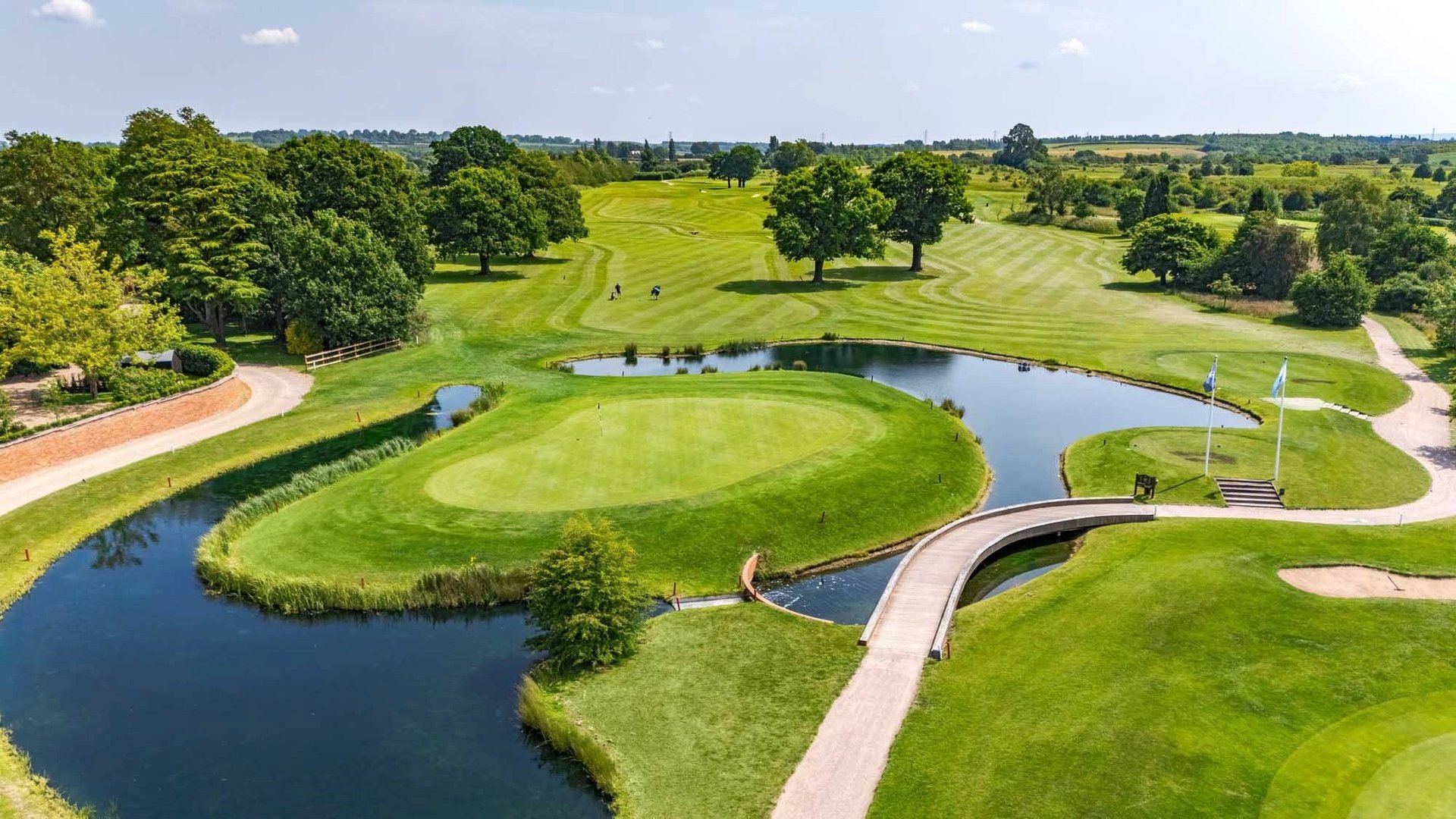 Aerial view of a manicured golf course with curved ponds, green fairways, and tree-lined landscape under blue sky