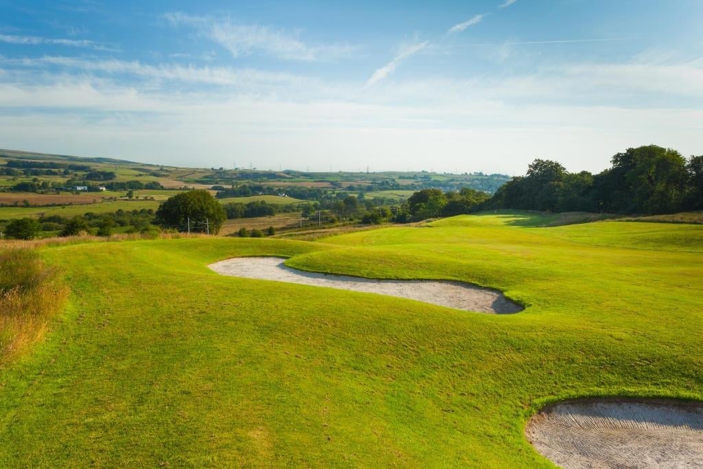 Golf course with water bunker and sand trap on rolling green fairway under blue sky