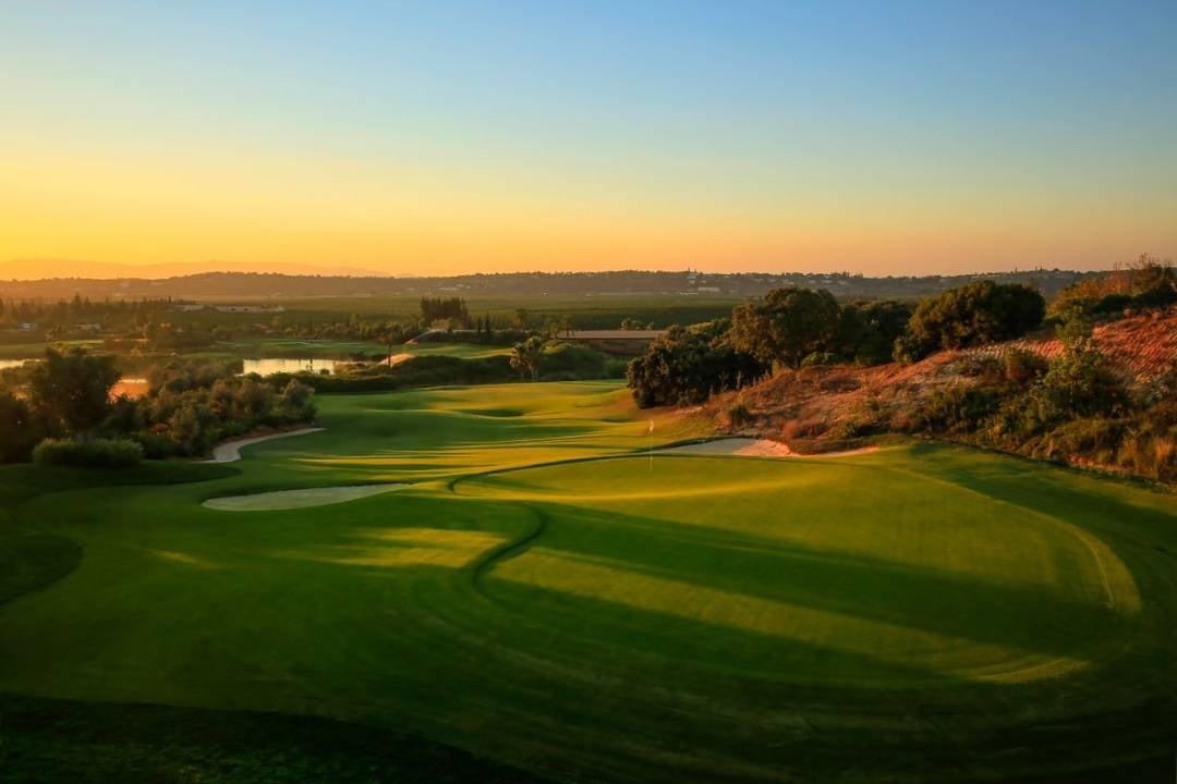Aerial view of a golf course with manicured fairways at sunset, surrounded by trees and rolling landscape