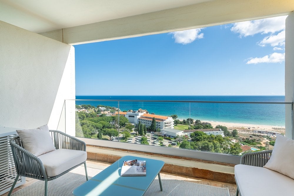 Modern balcony overlooking coastal beach town with blue ocean, sandy shore, and residential buildings under clear sky