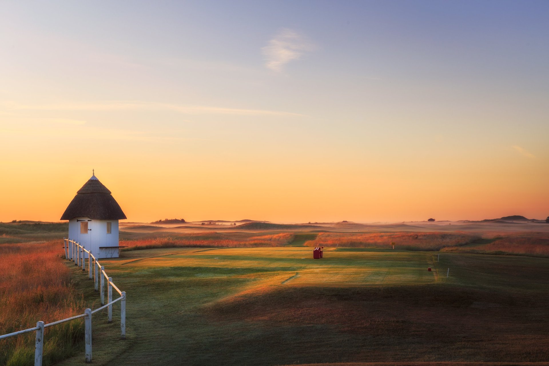 Windmill with conical roof in rural landscape at sunset with golden sky and green fields